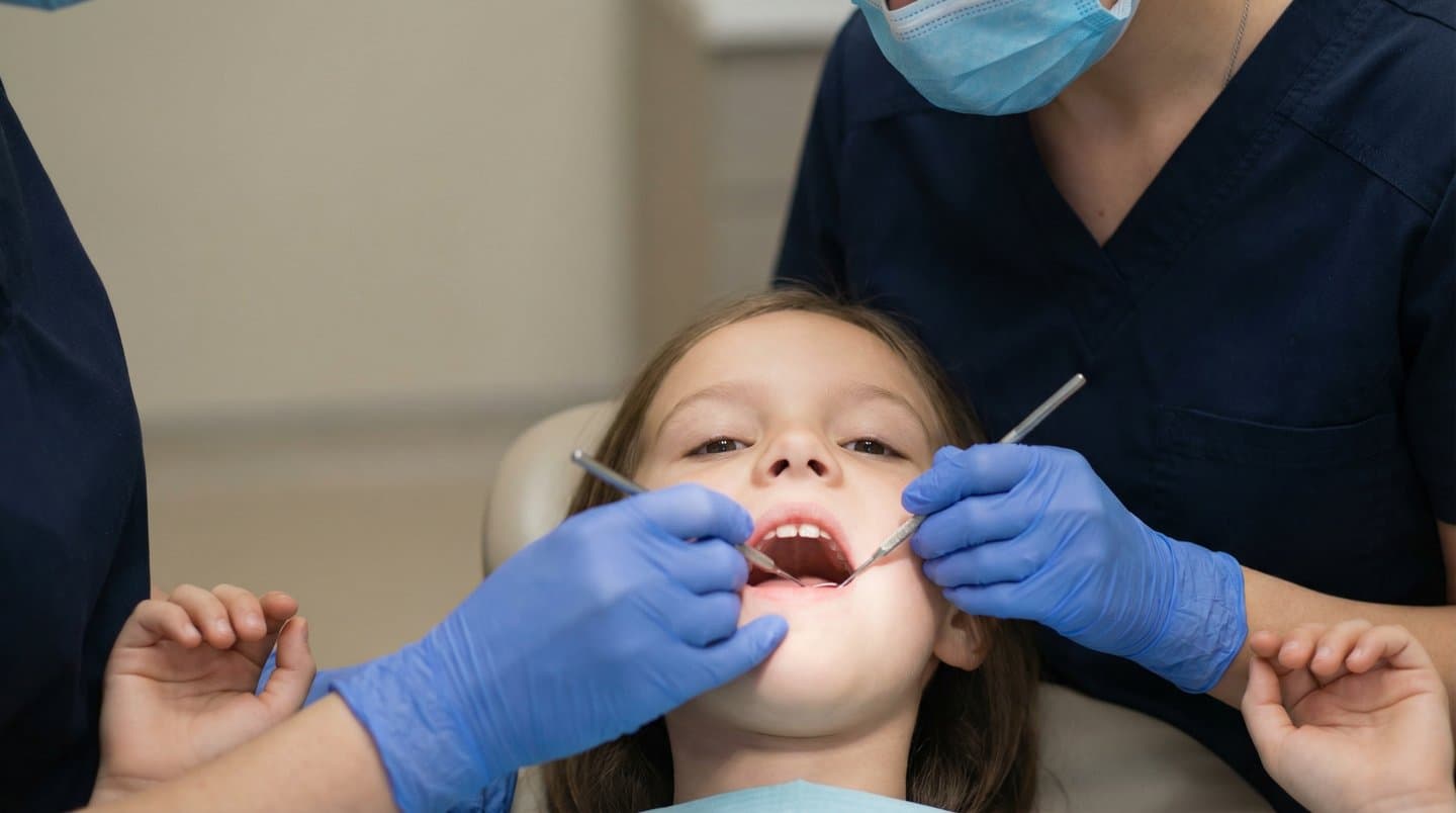 A calm child in a dental chair during an exam while clinicians use a mirror and explorer