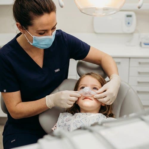 Clinician adjusting a nitrous oxide mask on a relaxed child during pediatric sedation dentistry
