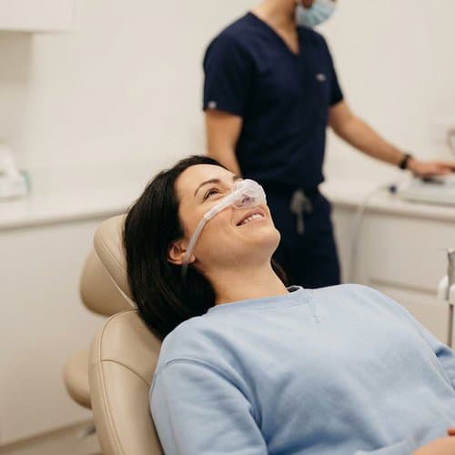 Clinician fitting a nitrous oxide nose mask while the patient smiles—sedation setup